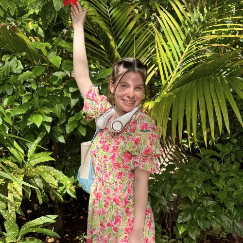 Caidance Bass, the baker behind The Bassy Baker, smiling in a floral dress among palm leaves