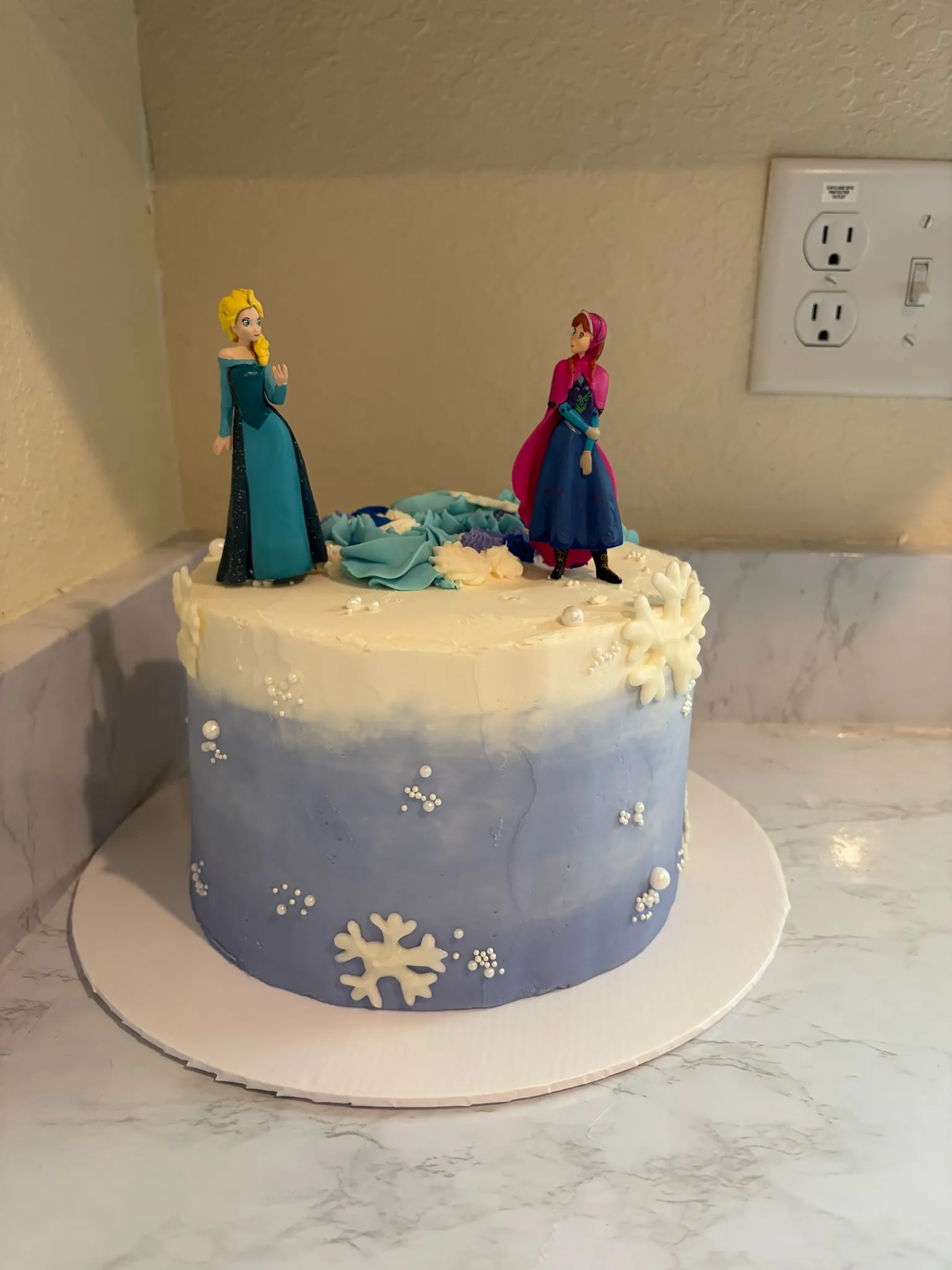 A blue ombre snowflake cake topped with Frozen figures
