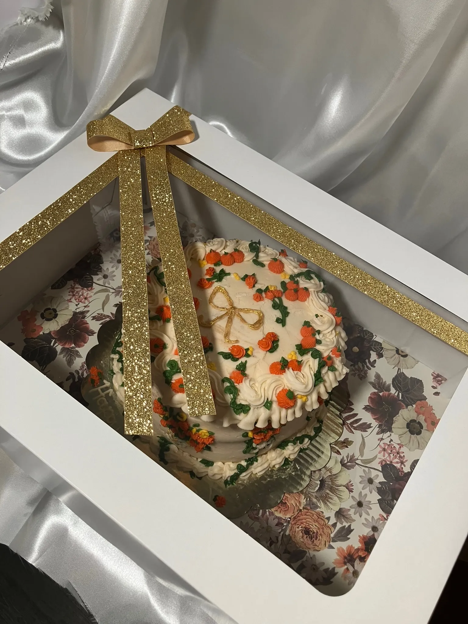 A cream cake finished with a gold ribbon bow and autumn decorations