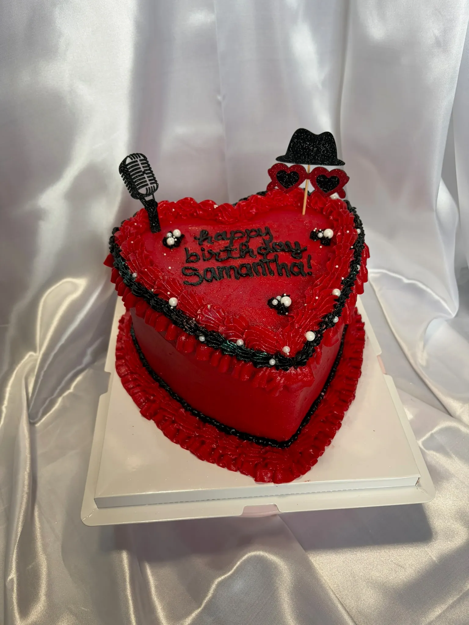 A red heart-shaped cake with ruffled piping and edible pearls