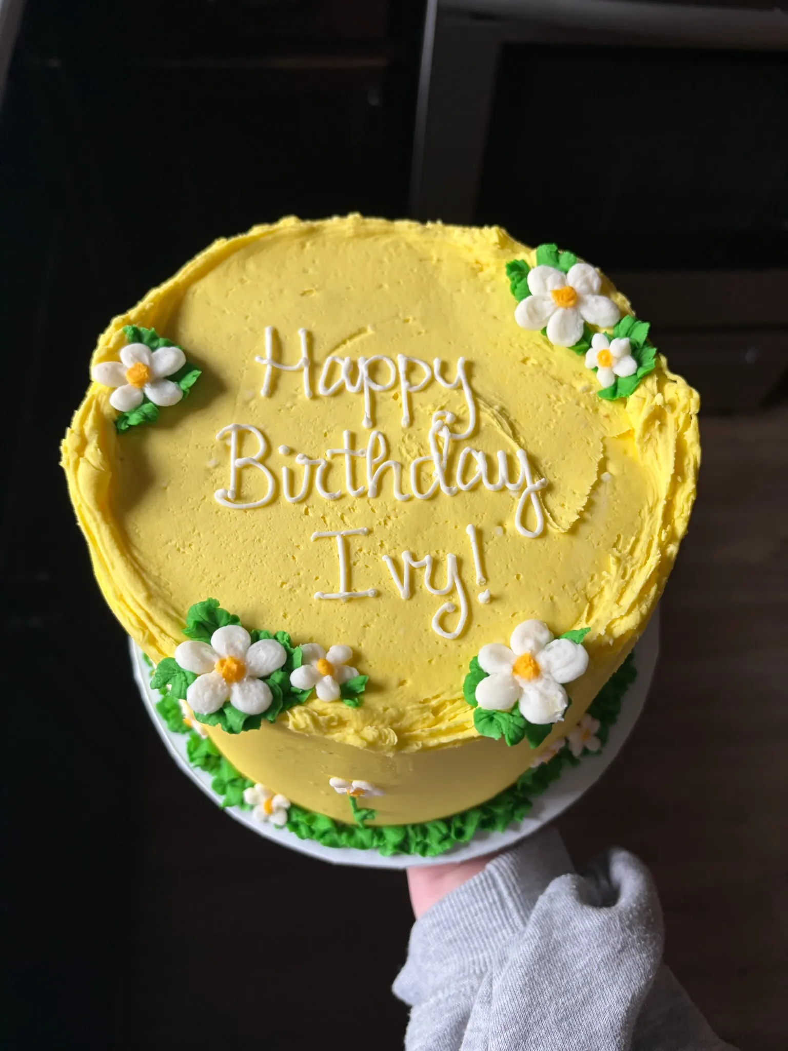 A yellow buttercream birthday cake trimmed with piped daisies