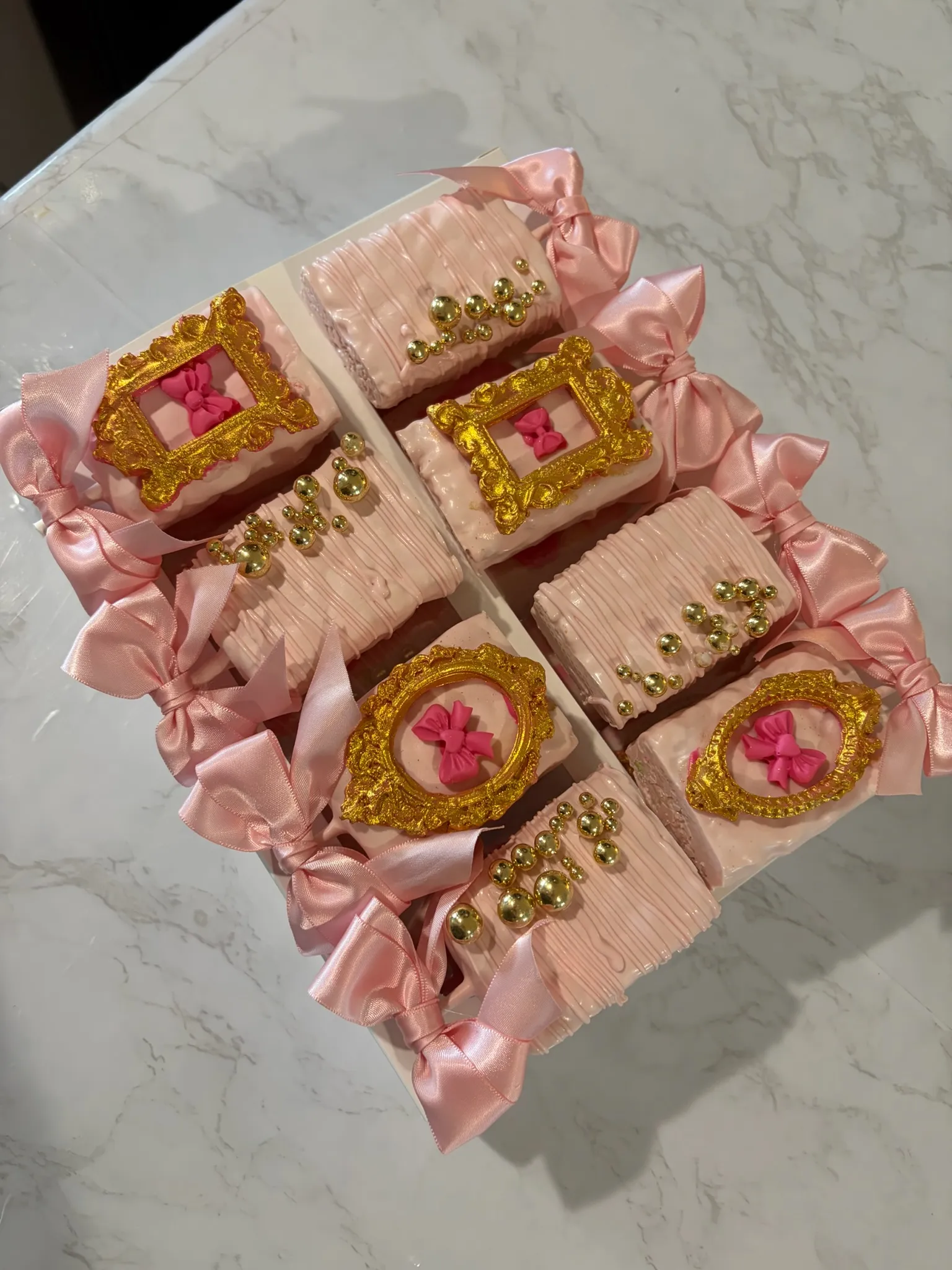 Pink and gold wrapped treats arranged in a ribboned box