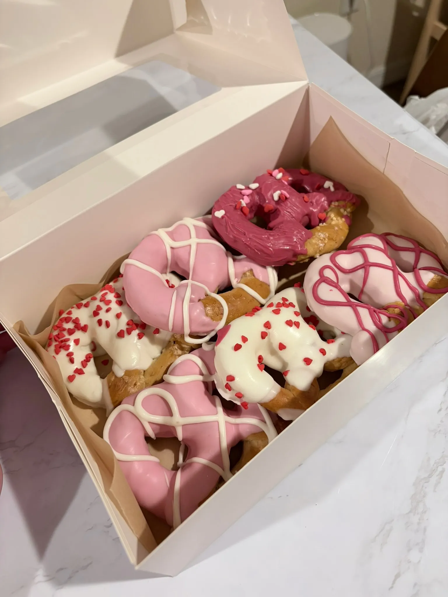 A box of pink and white drizzled treats decorated with sprinkles
